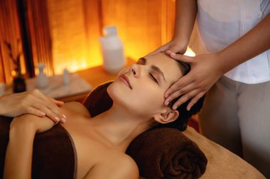 Beyaz kadın stres önleyici kafa masajı yapmaktan ve lüks otel veya otelde sıcak mum ışığında yüz güzelliği eğlencesi yapmaktan zevk alıyor. Sessiz.