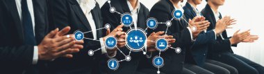 A group of business professionals applaud during a conference, surrounded by digital network icons, symbolizing collaboration and innovation in today corporate world. Amity