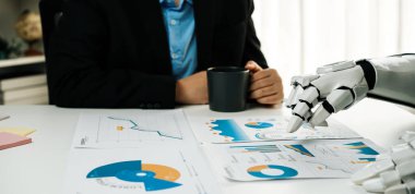 Bir iş adamı, çağdaş bir ofiste bir fincan kahvenin tadını çıkarırken, finansal raporları analiz ederek robotik teknolojiyle ilgilenir.