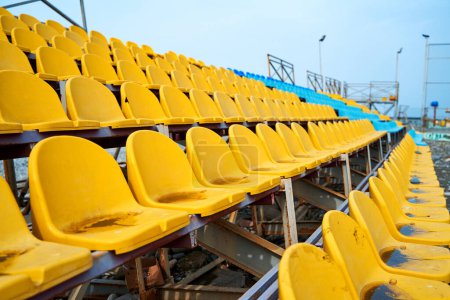 Téléchargez les photos : Sièges en plastique jaune sur le podium d'un petit terrain de sport. - en image libre de droit