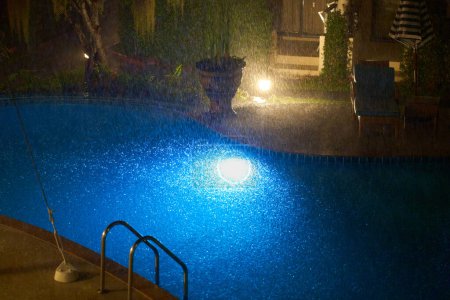 A heavy tropical downpour in the courtyard of the condo at night floods the pool.