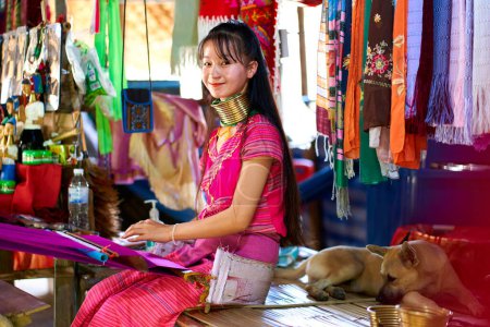 Téléchargez les photos : Portrait d'une femme d'une tribu à long cou, connue pour les anneaux métalliques autour de leur cou, tissant une couverture colorée. Célèbre la diversité culturelle et la tradition. Chiang Rai, Thaïlande - 02.09.2023 - en image libre de droit