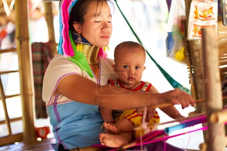Téléchargez les photos : Femme de la tribu à long cou, connue pour les anneaux métalliques portés autour de leur cou, tenant son enfant. La photo capture le lien entre la mère et l'enfant. Chiang Rai, Thaïlande - 02.09.2023 - en image libre de droit