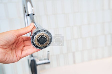 A woman is holding a chrome faucet covered with lime scale