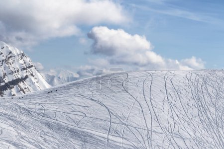 Foto de Nieve fuera de pista pendiente para freeriding con rastros de esquís, tablas de snowboard y silueta de freeriders en día de invierno soleado. Montañas del Cáucaso, Georgia, región Gudauri. - Imagen libre de derechos