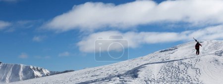 Photo for Skier with skis on his shoulder go up to top of mountain in cold sun day. Caucasus Mountains in winter, Georgia, region Gudauri, Mount Kudebi. Panoramic view. - Royalty Free Image