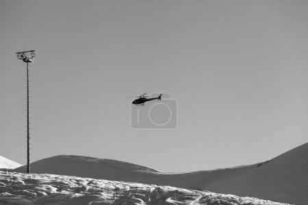 Foto de Helicopter in clear sky and snowy ski slope at sunny winter evening. Caucasus Mountains, Georgia, region Gudauri. Black and white toned landscape - Imagen libre de derechos