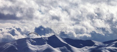 Foto de Vista panorámica de la montaña de la luz del sol de la noche con nubes y silueta de parapente. Montañas nevadas del Cáucaso en invierno. Georgia, región Gudauri. - Imagen libre de derechos