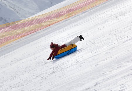 Foto de Young girl downhill on snow tube on ski resort at sunny day in snowy mountains. Winter vacation. - Imagen libre de derechos