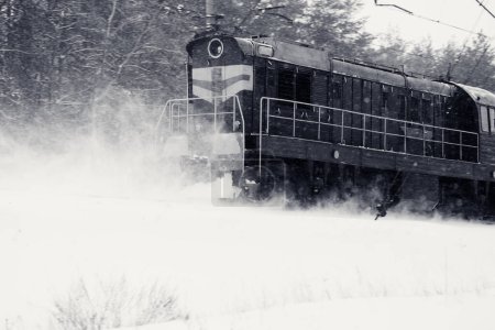 Foto de Tren cubierto de hielo paseos en tormenta de nieve a través del bosque de invierno nevado. Mal tiempo en el ferrocarril. Imagen retro tonificada en blanco y negro. - Imagen libre de derechos