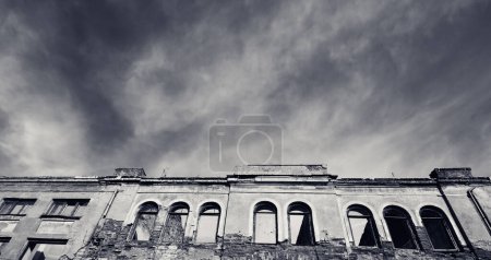 Téléchargez les photos : Panoramic view on facade of old destroyed house with broken windows and cloudy sky. Black and white retro toned image. - en image libre de droit