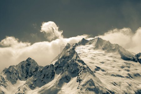 Foto de High winter snowy mountains in clouds. Caucasus Mountains, region Dombay, Mount Peak Ine. Retro color toned landscape. - Imagen libre de derechos