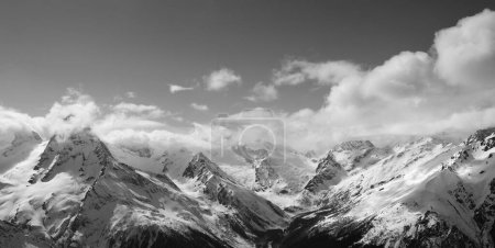 Schwarz-weißes Panorama von Bergen mit Sonnenlicht in Wolken. Kaukasus, Region Dombay im Winter.