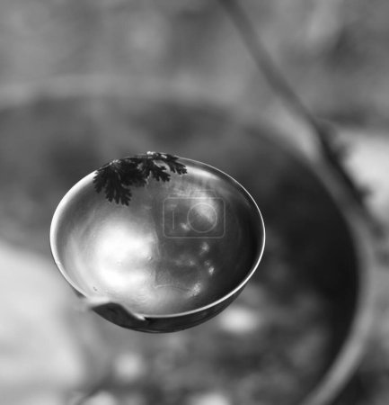 Photo for Black and white metal ladle (spoon) and soup in cauldron at background. Outdoor camping cooking. Selective focus. - Royalty Free Image