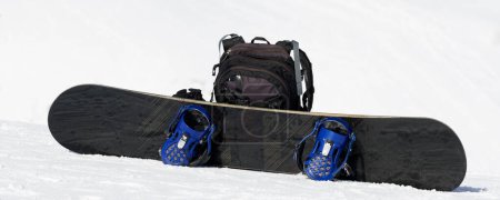 Foto de Snowboard y mochila negra en la pista de esquí en las montañas de nieve de invierno en un bonito día soleado. - Imagen libre de derechos