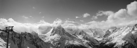 Téléchargez les photos : Panorama noir et blanc des montagnes enneigées ensoleillées dans les nuages et télésiège à la soirée ensoleillée d'hiver. Montagnes du Caucase, région Dombay. - en image libre de droit