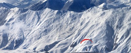 Foto de Parapente en las montañas nevadas sobre la estación de esquí y fuera de pista en la soleada noche de invierno. Montañas del Cáucaso. Georgia, región Gudauri. Vista panorámica. - Imagen libre de derechos