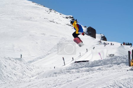 Photo for DOMBAY,  APRIL, 2010: Flammable Camp Dombai 2010. Snowboarder jumping in snow park at ski resort on sunny winter day. Caucasus Mountains, region Dombay. - Royalty Free Image