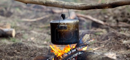 Photo for Cooking in sooty cauldron on campfire at forest. Panoramic view. - Royalty Free Image