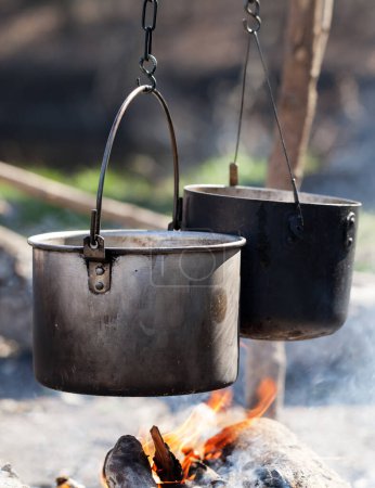 Photo for Cooking in two sooty old cauldrons on bonfire with smoke at forest in sunny summer day. Close-up view. - Royalty Free Image