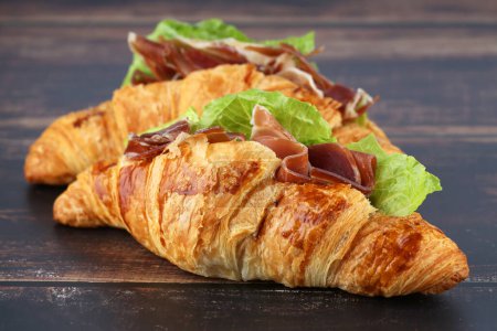 Foto de Sandwiches de croissant con jamón y lechuga sobre mesa de madera. - Imagen libre de derechos