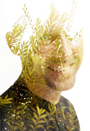Téléchargez les photos : Un portrait d'un homme souriant, combiné à une photo de branches vertes fraîches en double exposition technique, disparaît en arrière-plan - en image libre de droit