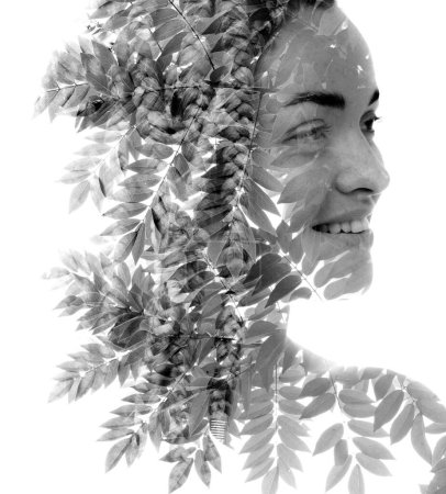 Téléchargez les photos : Portrait en demi-profil noir et blanc d'une femme souriante disparaissant dans une photo désaturée de feuilles d'arbre en double exposition - en image libre de droit