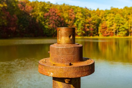 Téléchargez les photos : Vue rapprochée du tuyau métallique rouillé et de la vanne sur une jetée dans un réservoir calme dans la forêt d'État de Coopers Rock près de Morgantown, au Wisconsin, alors que les feuilles d'automne fournissent le fond - en image libre de droit