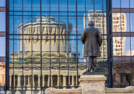 Monumento a McKinley frente a un reflejo del edificio del Capitolio del estado de Ohio en las ventanas de un edificio de oficinas al otro lado de la calle en Columbus, OH
