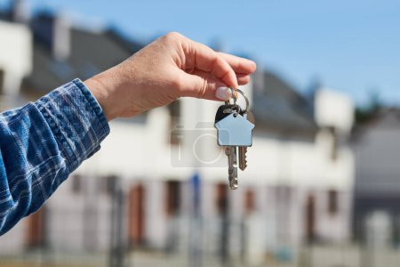 Téléchargez les photos : Porte-clés main sur porte-clés devant une nouvelle maison. Projet de construction, déménagement dans une nouvelle maison, hypothèque, loyer ou achat immobilier. - en image libre de droit