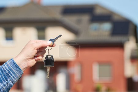 Téléchargez les photos : Porte-clés main sur porte-clés devant une nouvelle maison. Projet de construction, déménagement dans une nouvelle maison, hypothèque, loyer ou achat immobilier. - en image libre de droit