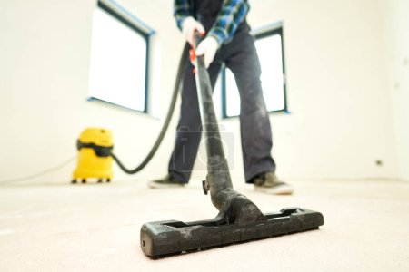 Téléchargez les photos : Ouvrier nettoyer et enlever la poussière de construction avec aspirateur pendant la réparation ou la rénovation - en image libre de droit