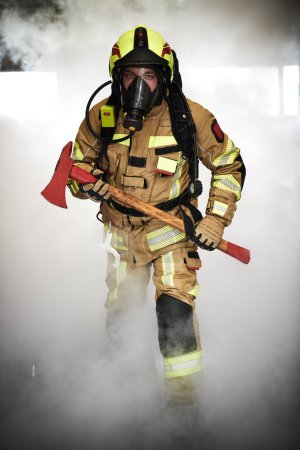 Foto de Bombero con hacha en protección desgaste en el trabajo caminando a través del humo. - Imagen libre de derechos