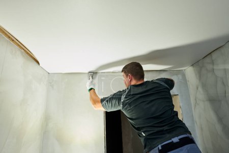 Téléchargez les photos : Travailleur contractuel installant un plafond tendu dans la salle de bain. Services de rénovation et de construction - en image libre de droit