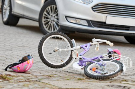 Foto de Casco de ciclismo infantil en la calle junto a una bicicleta después de un accidente de coche en la ciudad - Imagen libre de derechos
