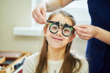 Téléchargez les photos : Test de vue d'enfant. Jeune fille avec phoropter lors des examens oculaires en clinique ophtalmologique. BeH3althy - en image libre de droit