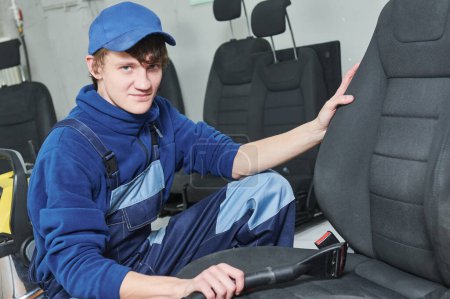 Téléchargez les photos : Service de nettoyage de sièges en tissu automobile. Portrait du travailleur avec aspirateur pendant les détails de la voiture - en image libre de droit