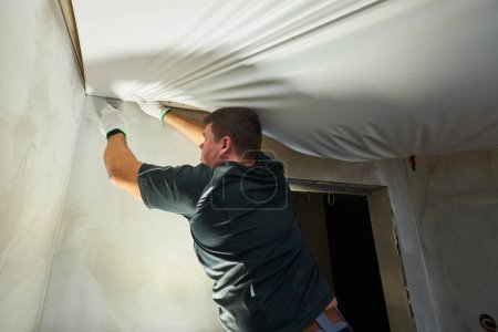 Travailleur contractuel installant un plafond tendu dans la salle de bain. Services de rénovation et de construction