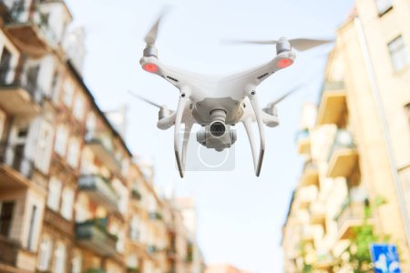 Téléchargez les photos : Drone avec appareil photo numérique volant ou planant dans la rue de la ville - en image libre de droit