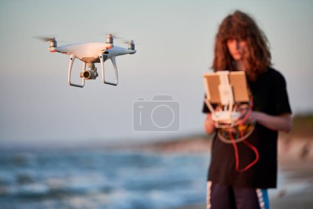 Foto de Hombre operando dron al atardecer. Drone volando sobre un mar. Concéntrate en drone - Imagen libre de derechos