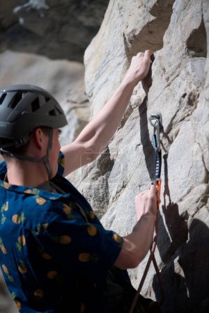 Téléchargez les photos : Homme grimpeur accroché à la paroi rocheuse tandis que attaché sur - en image libre de droit