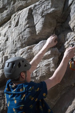 Téléchargez les photos : Vue latérale du grimpeur mâle une main tenant la roche autre main attachant le tirage rapide - en image libre de droit