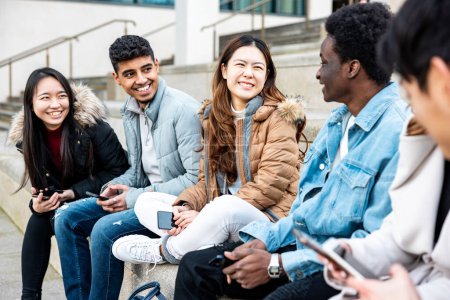 Photo for Authentic shot of happy group of multiracial friends millennials and generation z people in the city using mobile phones and laughing together - Friendship and lifestyle concepts - Royalty Free Image