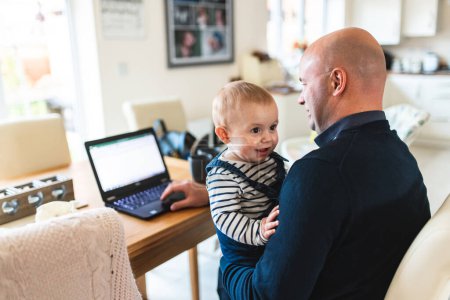 Foto de Happy baby boy with hid father working from home - Man and son together in the living room - Concepts of remote work, children, parenthood, lifestyle in the UK - Imagen libre de derechos