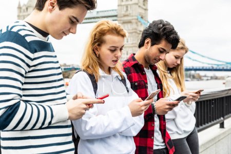 Téléchargez les photos : Groupe d'étudiants adolescents à Londres en utilisant le téléphone près de Tower Bridge - Groupe multiracial d'adolescents meilleurs amis profiter du temps ensemble à Londres - Mode de vie et amitié à Londres - en image libre de droit