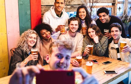 Téléchargez les photos : Amis heureux de prendre un selfie de groupe au pub - Groupe de personnes multiraciales milléniaux s'amuser ensemble au pub et prendre une photo - Anniversaire ou après le travail réunion, le bonheur et le travail d'équipe concepts - en image libre de droit