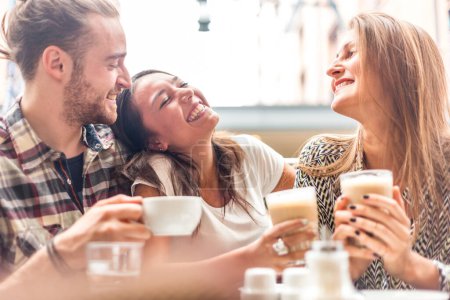 Téléchargez les photos : Groupe multiracial d'amis prenant un café ensemble - Deux femmes et un homme au café, parlant, riant et appréciant leur temps - Concept de style de vie et d'amitié avec des modèles de personnes réelles - en image libre de droit