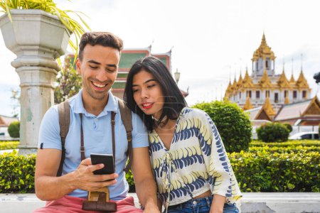 Foto de Feliz pareja multirracial o amigos en Bangkok comprobando por teléfono - Gente de raza mixta divirtiéndose juntos en vacaciones en verano - Viajes y conceptos de estilo de vida - Imagen libre de derechos