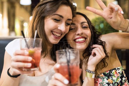 Photo for Two happy women best friends enjoying a drink together on a night out in the city in summer - Lifestyle and friendship concepts of happy people in Italy with alcoholic drinks - Royalty Free Image