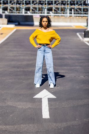 Photo for Woman portrait standing in front of an arrow pointing at her - Beautiful multiracial young woman wearing yellow top and curly hair - determination and lifestyle concepts - Royalty Free Image